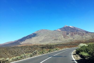 Country road leading towards mountains against blue sky