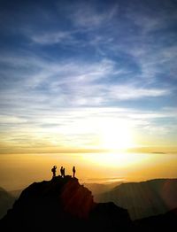 Silhouette people standing on rock against sky during sunset