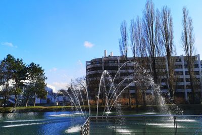 Fountain by river in city against sky