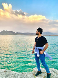 Full length of young man standing in sea against sky