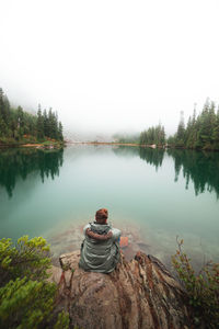 Rear view of man sitting by lake against clear sky