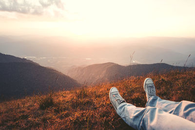 Low section of man on mountain against sky during sunset