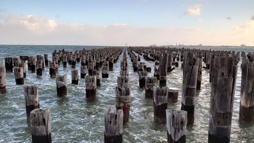 Wooden posts in sea against sky