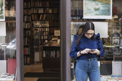 Woman using smart phone while standing outside bookstore