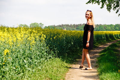 Young woman walking by yellow flowers on oilseed rape field