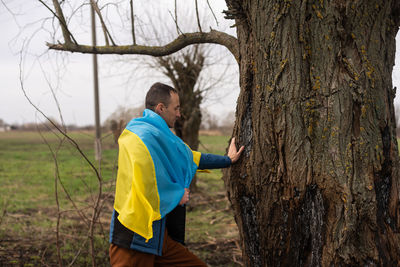 Side view of man standing by tree trunk