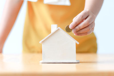 Close-up of hand holding coin by model house