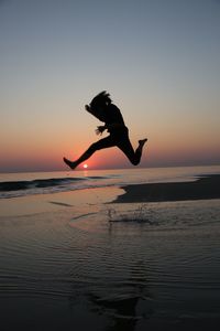 Man jumping in sea against sky during sunset