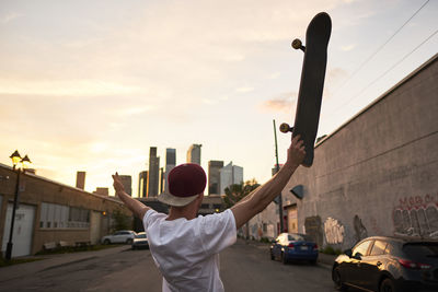 Young skateboarder holding board in air looking towards downtown