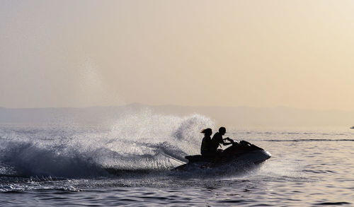 Couple riding jet boat on sea against clear sky