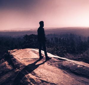 Rear view of silhouette man standing on rock at sunset