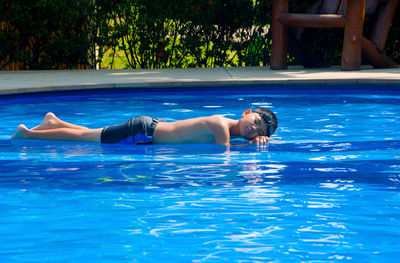 Full length of shirtless boy lying on swimming pool