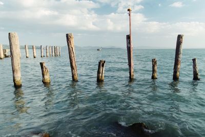 Wooden posts in sea against sky