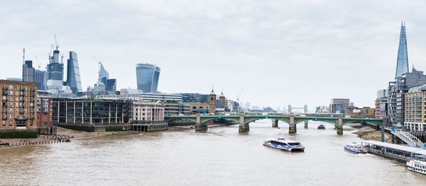 Bridge over river by buildings against sky in city