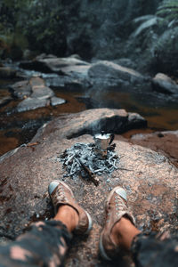 Low section of person sitting on rock by river