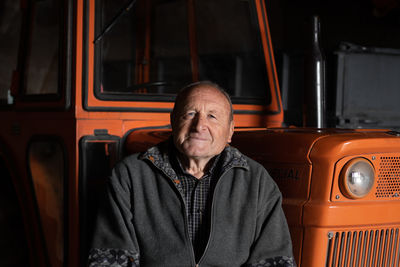 Portrait of senior man sitting by vehicle outdoors