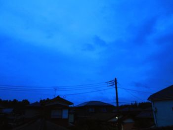 Silhouette houses and electricity pylon against sky at dusk