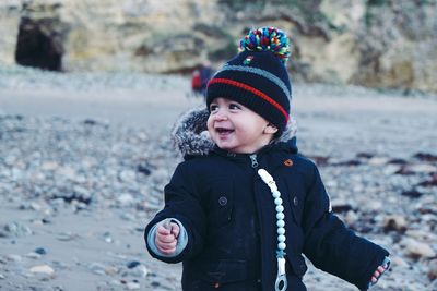 Cute happy baby boy looking away while standing at beach