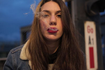 Close-up portrait of young woman smoking cigarette outdoors