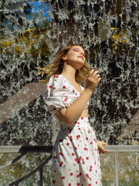 Portrait of young woman standing against waterfall