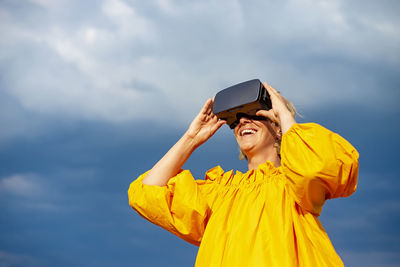 Woman wearing vr glasses standing against sky