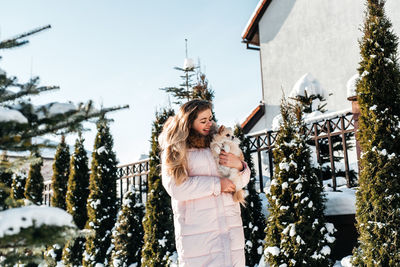 Woman standing on snow covered plants against trees during winter