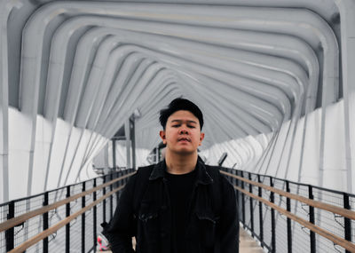 Portrait of young man standing against bridge