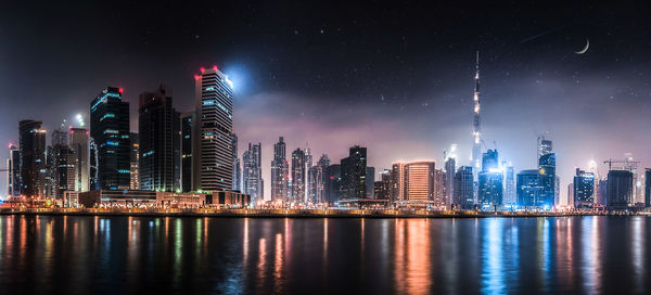 Illuminated modern buildings in city against sky at night