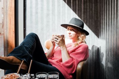 Woman sat thinking whilst drinking a hot drink in a cafe in fall