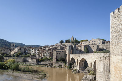 Buildings by river against clear blue sky