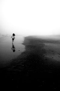 Rear view of woman running at beach during foggy weather