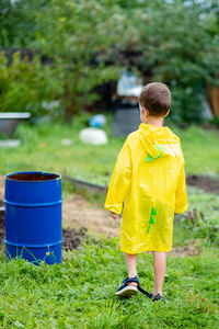 A boy in a yellow raincoat walks in the rain, back view. a child on the street. bright clothes.