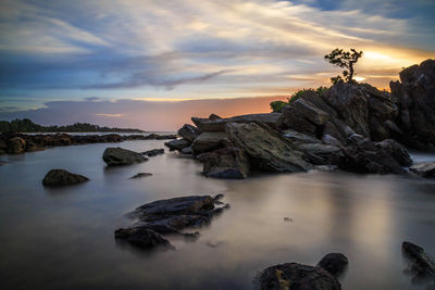 Rocks by sea against sky during sunset