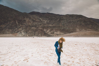 Young woman holding camera walking at death valley national park against sky