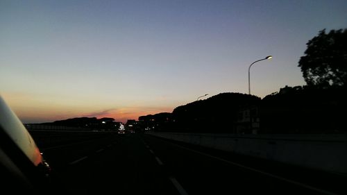 Cars on street against clear sky at sunset