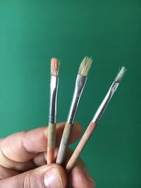 Cropped image of hand holding paintbrushes against green background