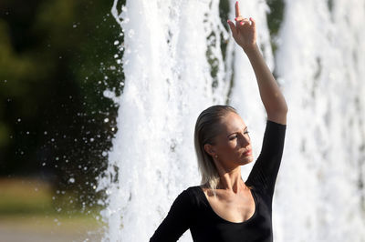 Beautiful woman with hand raised standing against fountain