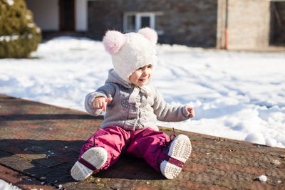 Full length of baby girl sitting on footpath in snow