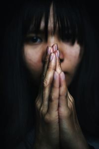 Close-up portrait of young woman with hands clasped against black background