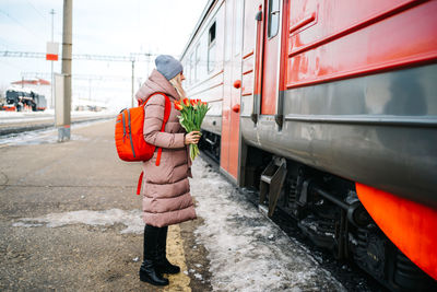 Girl on the platform of the station with a red backpack and a bouquet of tulip flowers