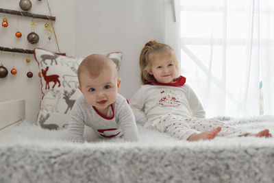 Brother and sister in christmas pajamas are sitting on the bed.