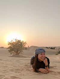 Smiling young woman on beach against sky during sunset