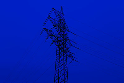 Low angle view of electricity pylon against clear blue sky