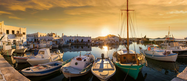 Boats moored in harbor at sunset