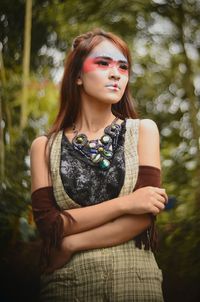 Thoughtful young woman with face paint looking away while standing in forest