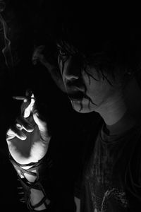 Close-up of young man with spooky face paint smoking in darkroom