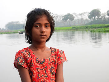 Portrait of young woman standing against lake