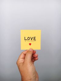 Cropped hand of person holding text on adhesive note against gray background