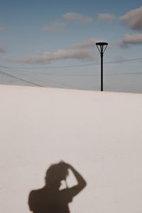 Shadow of person on street light against sky