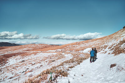 Rear view of person walking on snowcapped mountain against sky